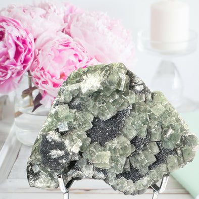 Mineral specimen on a stand with pink flowers in the background